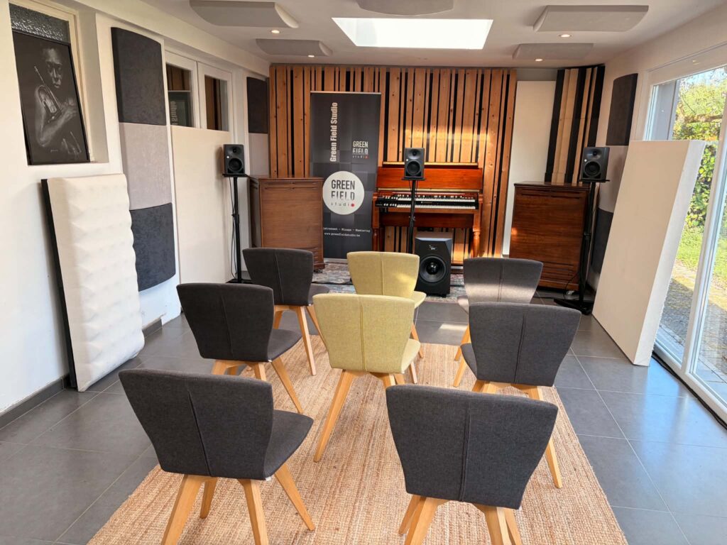 La salle d'écoute du Green Field Studio avant une session : des chaises face à un écran, des enceintes de studio de chaque côté et un mur de lattes de bois au fond.