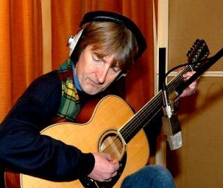 Portrait d'Anthony Phillips jouant de la guitare 12 cordes en studio, casque sur les oreilles