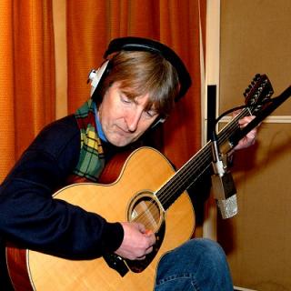 Portrait d'Anthony Phillips jouant de la guitare 12 cordes en studio, casque sur les oreilles