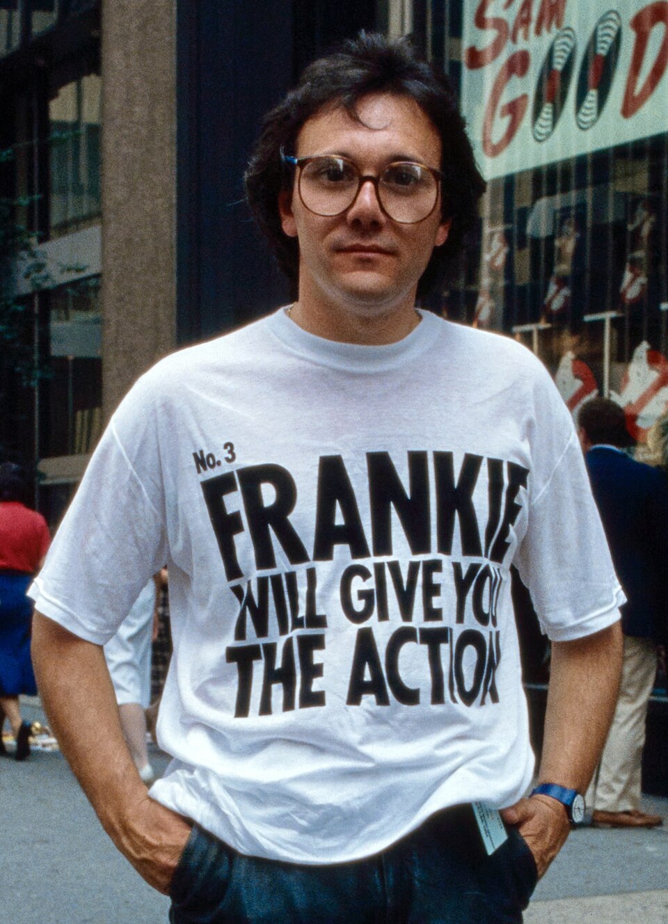 Trevor Horn en 1984 dans une rue de New York, avec des lunettes et un t-shirt blanc au slogan de Frankie Goes to Hollywood